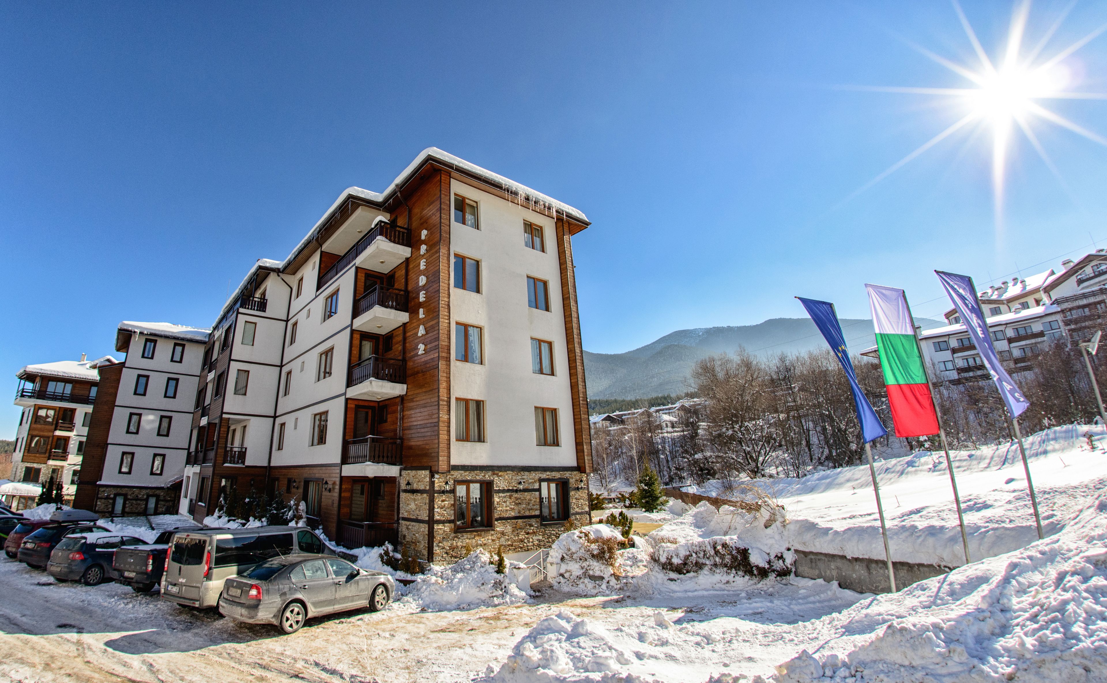 A multi-story hotel with balconies, a parking area, and flags.