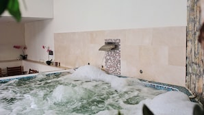 Un espace spa comprenant un bain à remous, des murs carrelés et un coin salon avec des chaises et une table.