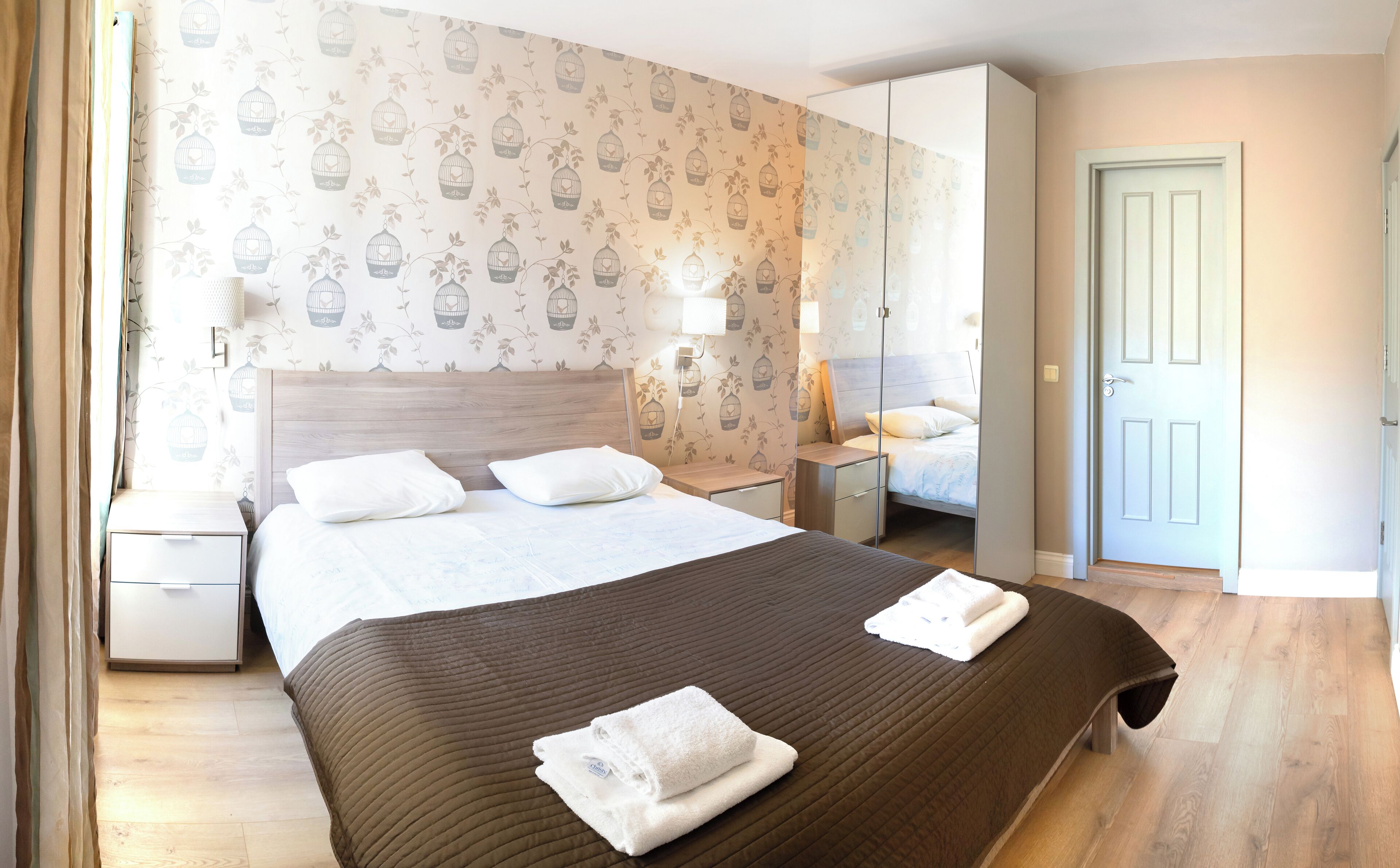 A hotel room with a large bed, two bedside tables, a wardrobe, and a door.