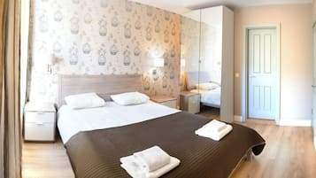 A hotel room with a large bed, two bedside tables, a wardrobe, and a door.