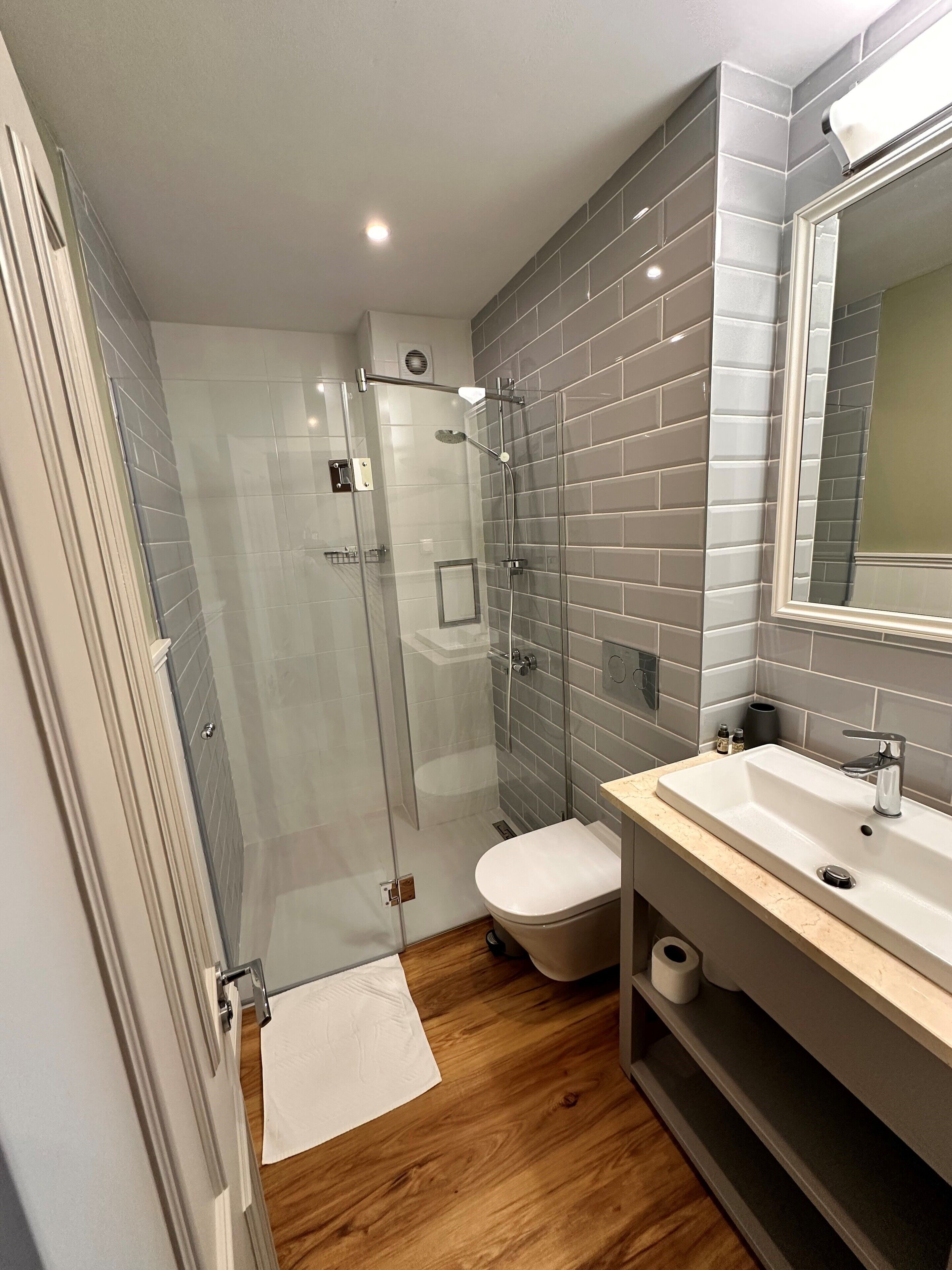 A modern bathroom with a glass shower enclosure, a white toilet, and a vanity with a sink and mirror.