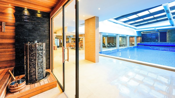 Une piscine intérieure moderne avec un mur en verre, un espace sauna avec un mur en pierre et un plafond en bois.