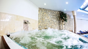 Un bain à remous avec un mur de pierres en arrière-plan, un verre de vin rouge et une plante en pot.