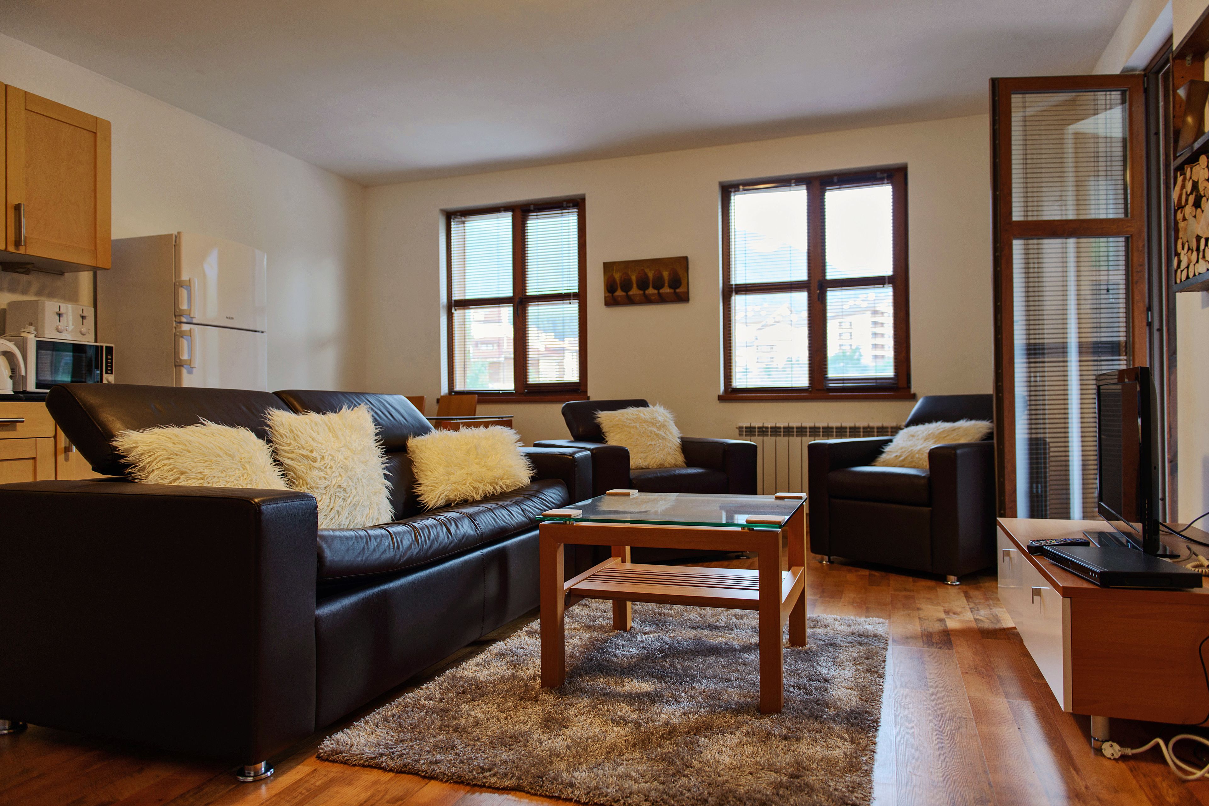A modern living room with a black leather sofa, a glass coffee table, and a wooden cabinet.