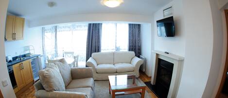 A living room with a sofa, a coffee table, a fireplace, and a TV mounted on the wall.