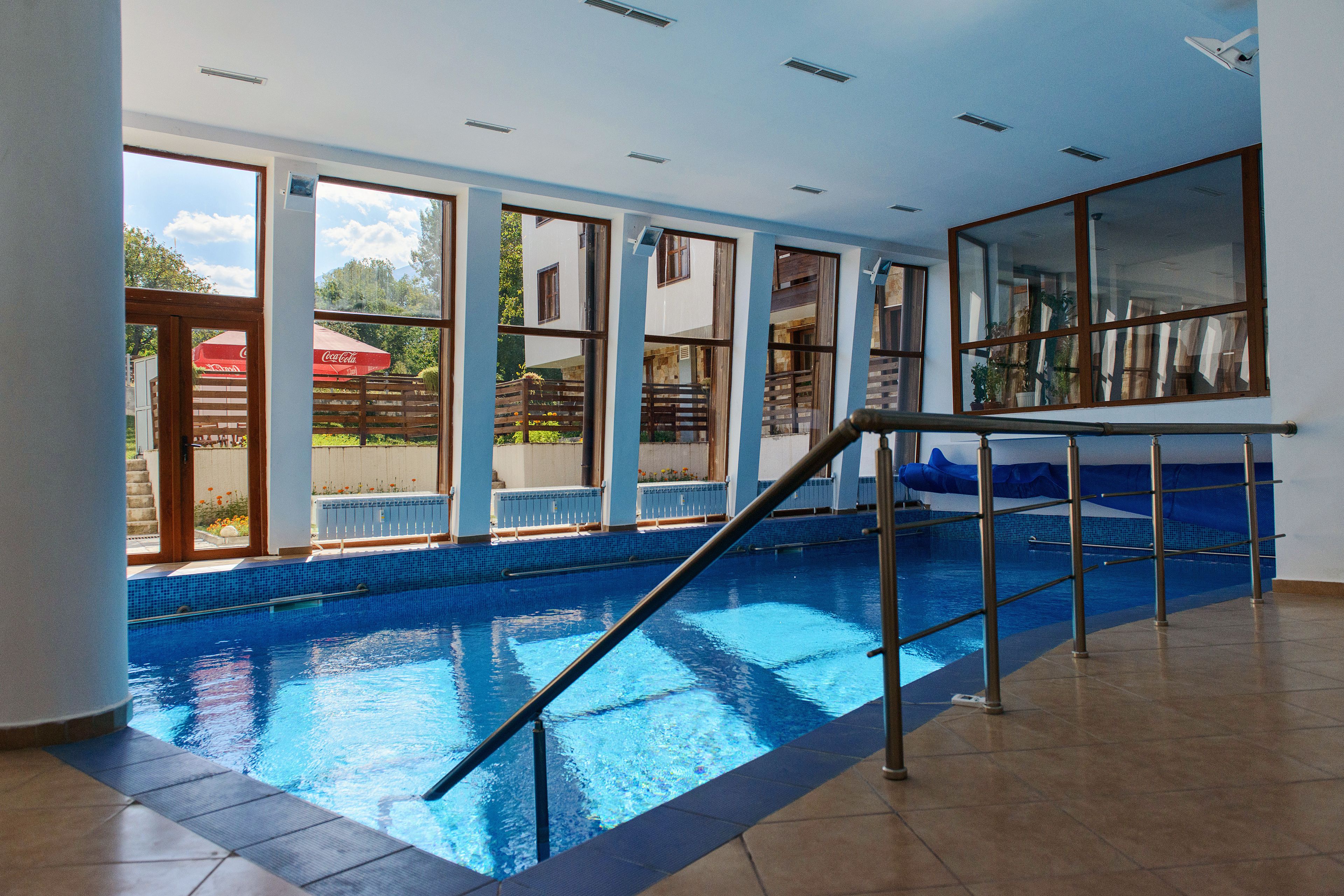 Una piscina interior con agua cristalina azul, ventanas amplias y una escalera de metal.