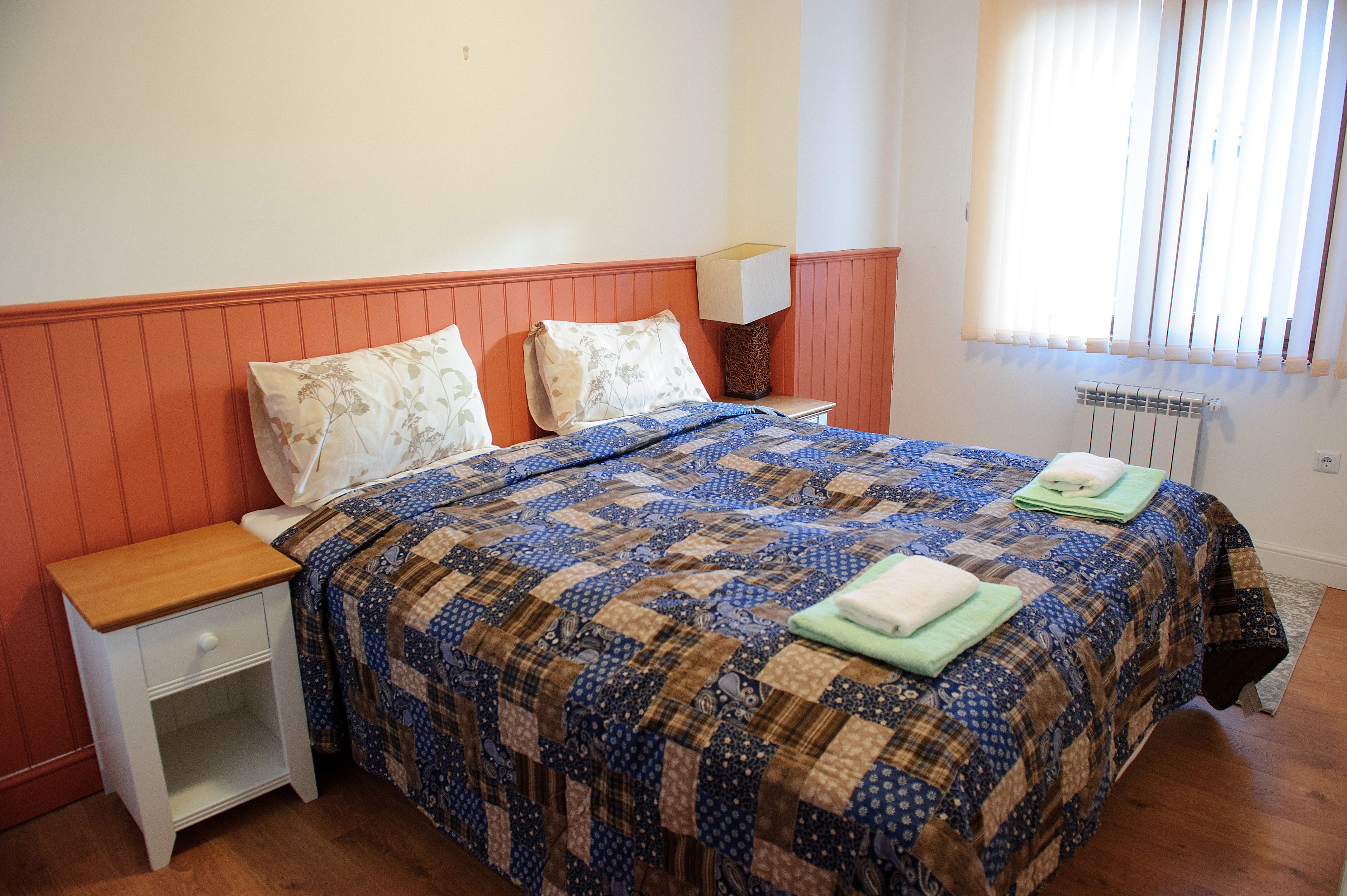 Un dormitorio con cama, mesita de noche, lámpara y radiador.