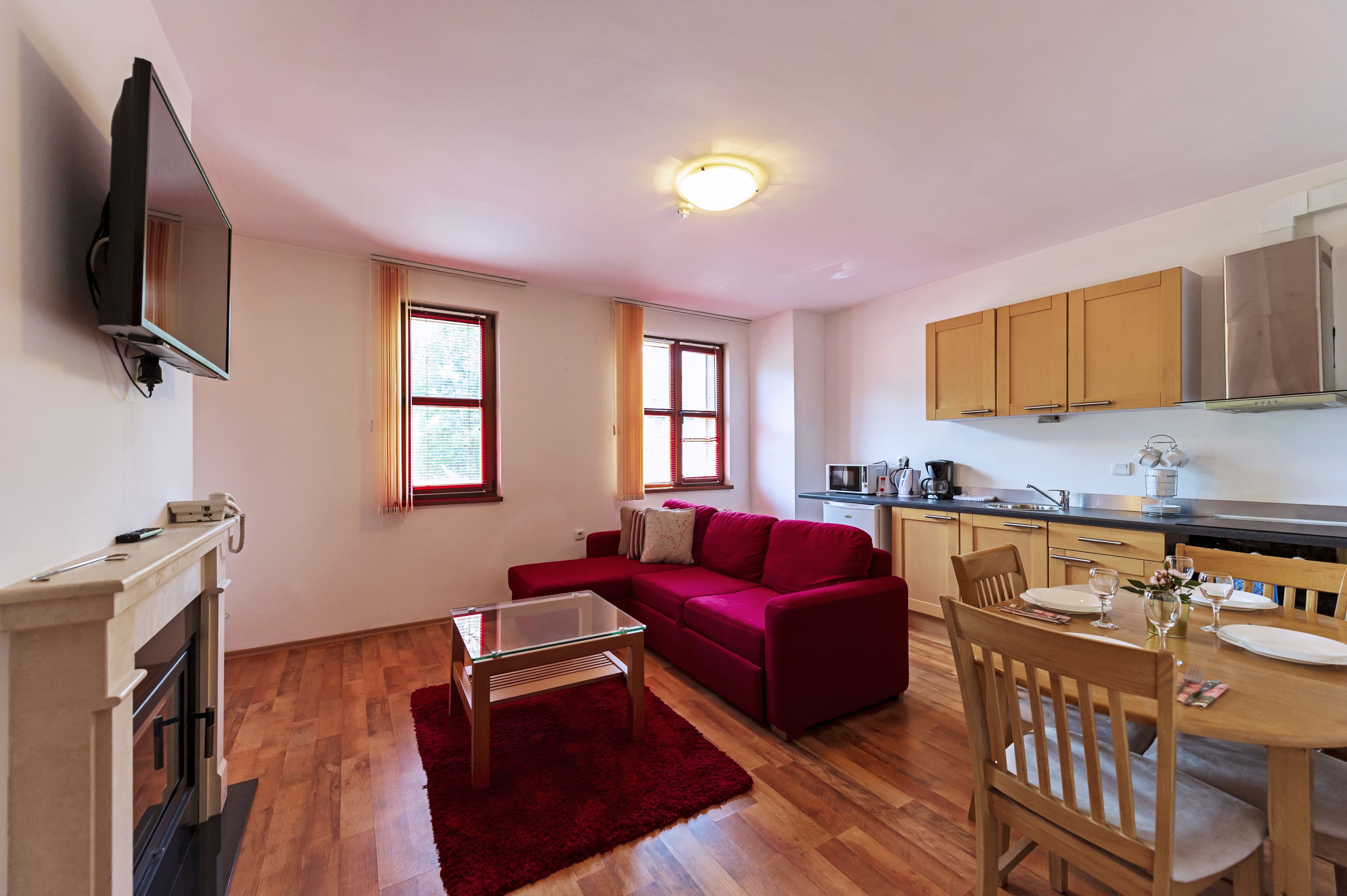 Un espacio habitable compacto con sofá, mesa de comedor, televisor montado en la pared y cocina equipada con armarios y microondas.