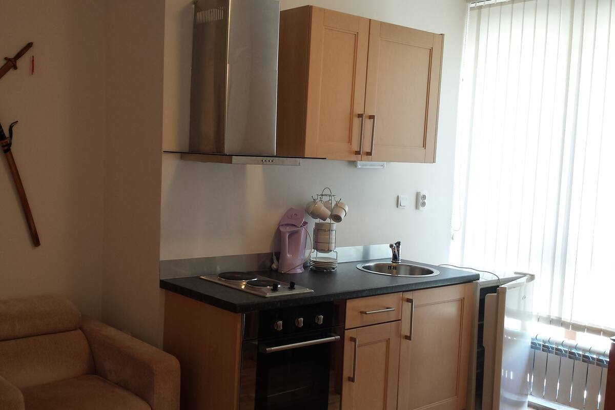 A kitchen with wooden cabinets, a stove, a sink, and a chair.