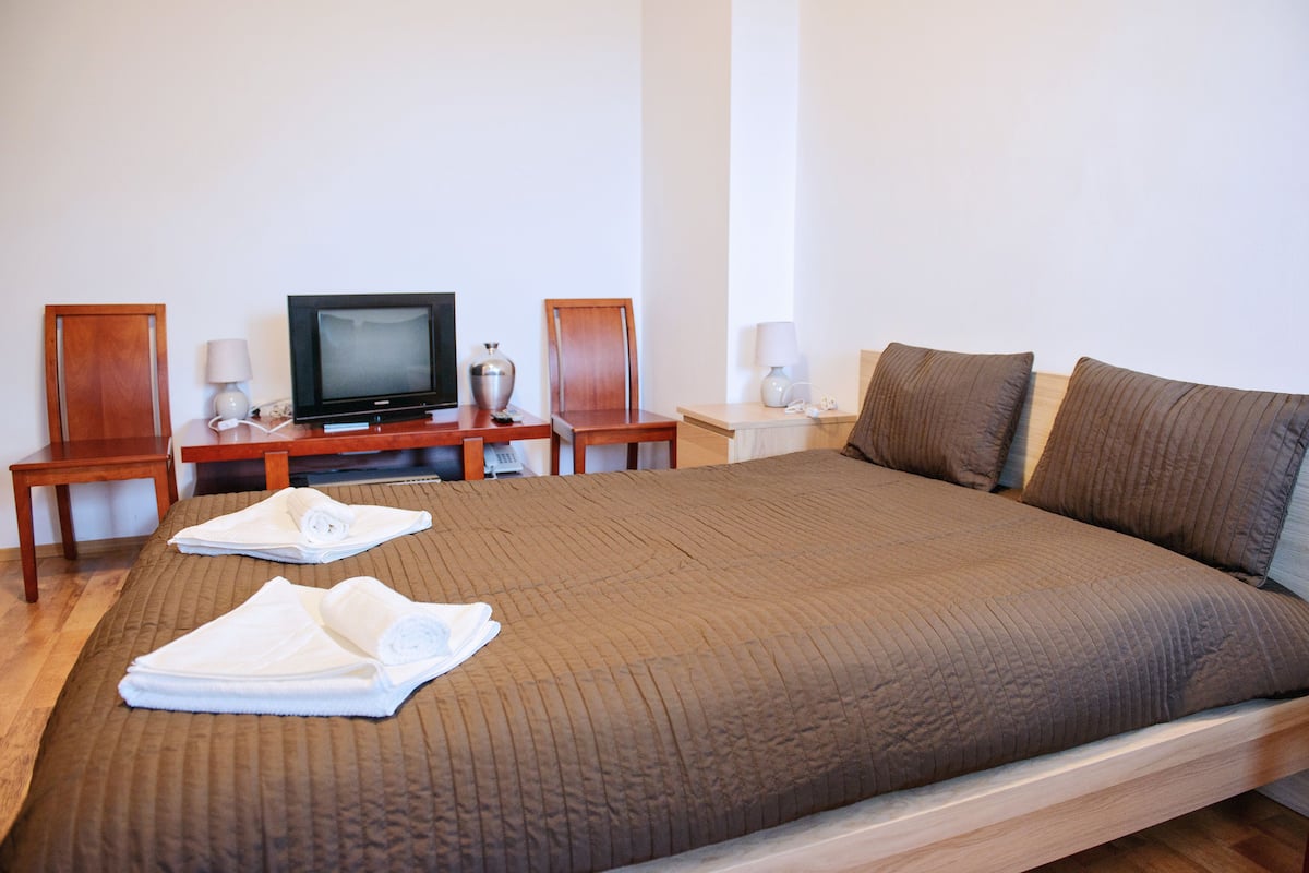 A hotel room with a large bed, a television, two nightstands, and a wooden desk.