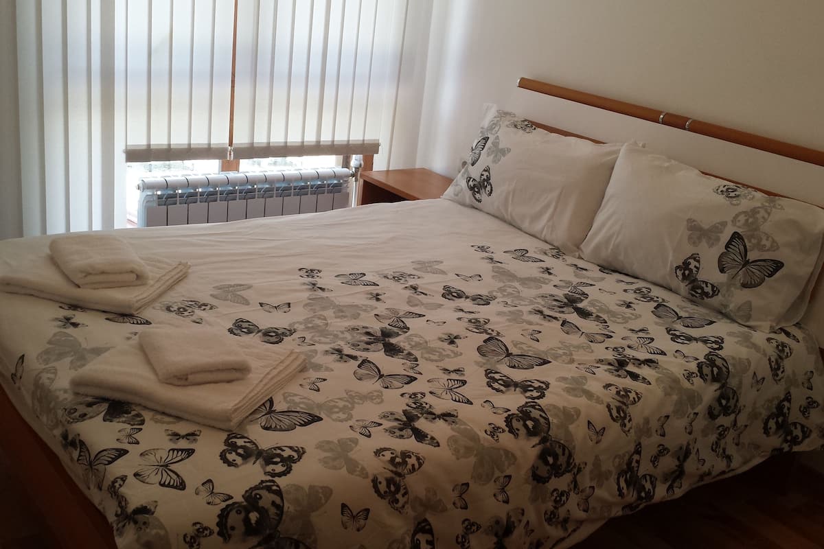 A neatly made bed with a floral and butterfly pattern, two folded towels, and a wooden headboard.