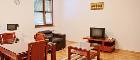 Una sala de estar con una mesa de comedor, sillas, un sofá, un televisor, un reloj y una ventana con persianas.