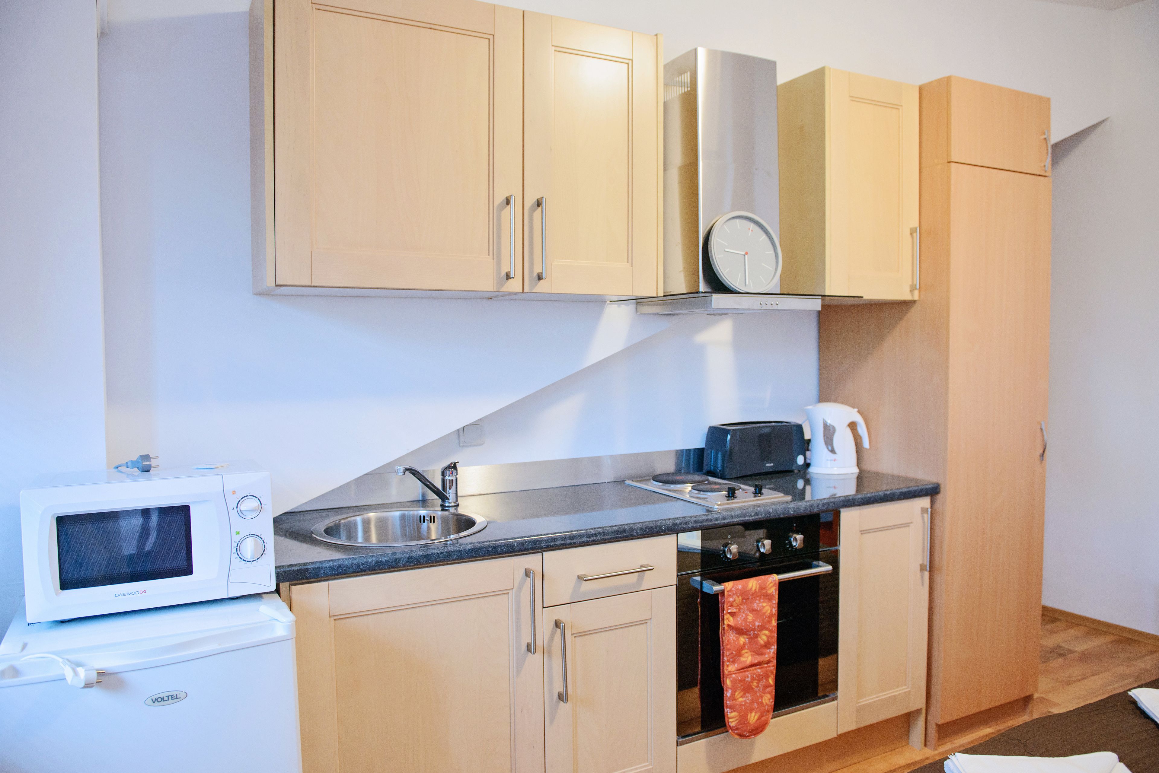 A compact kitchen with wooden cabinets, a microwave, a toaster, and a kettle.