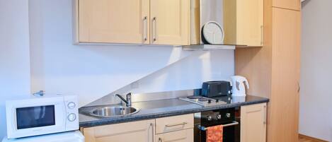 A compact kitchen with wooden cabinets, a microwave, a toaster, and a kettle.