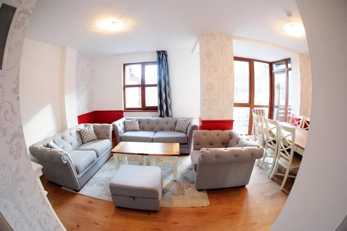 A living room with a grey sofa set, a coffee table, and a dining area with white chairs.