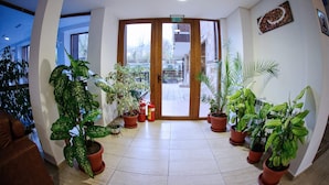 A hotel lobby with a curved ceiling, potted plants, a fire extinguisher, and a view of the outside through glass doors. - Mountain View Resort (Bansko)