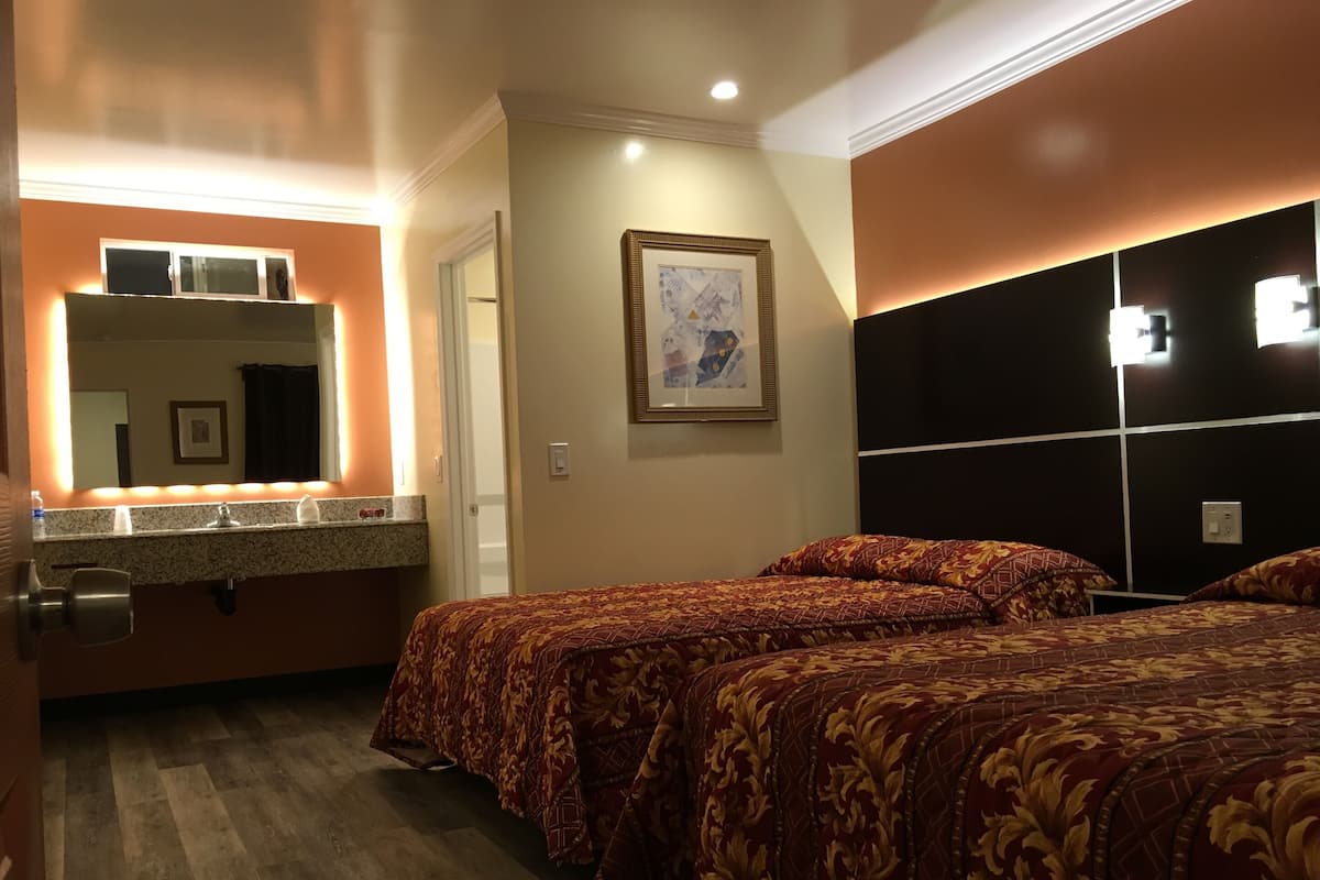 Habitación de hotel con dos camas, baño con tocador y un cuadro grande en la pared.