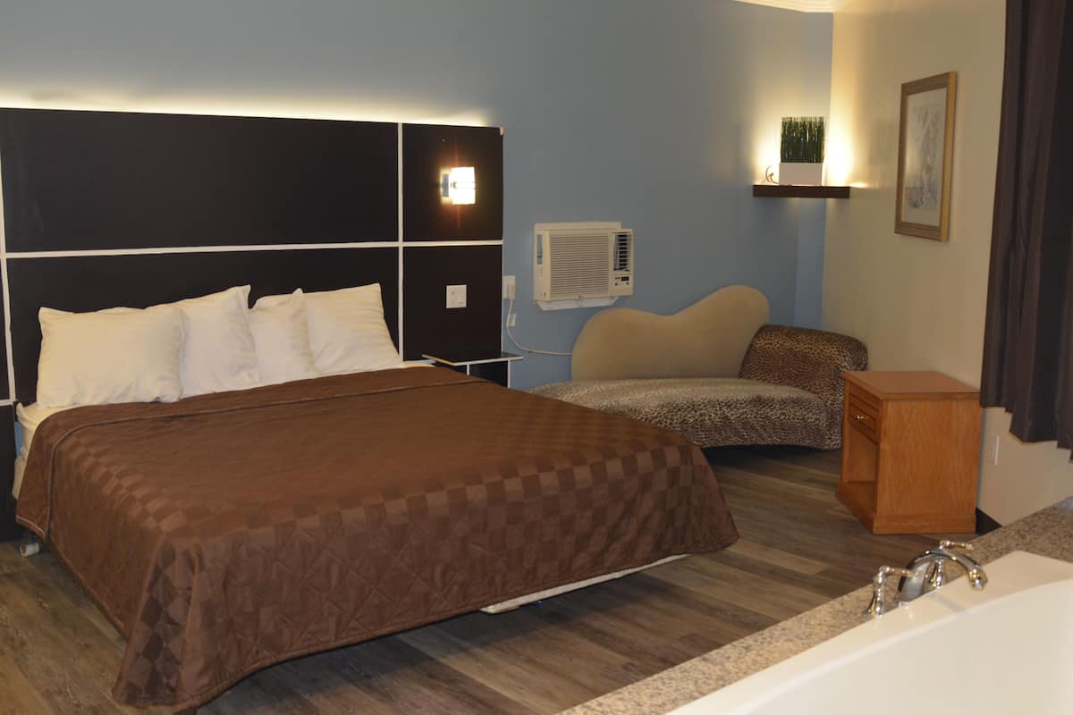 Habitación de hotel con una cama grande, un sofá, una mesita de noche de madera, un aire acondicionado montado en la pared y un cuadro en la pared.