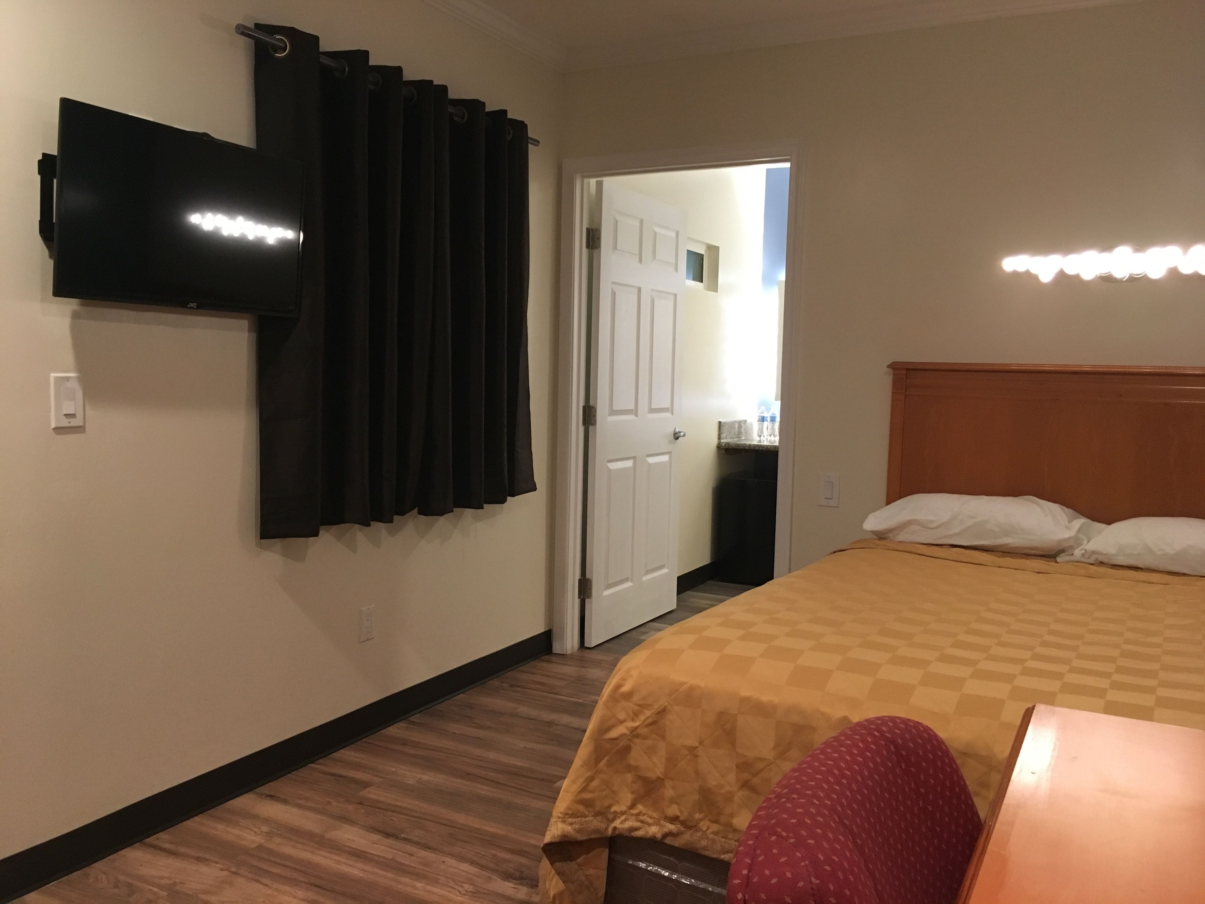 Habitación de hotel con cama, televisor montado en la pared, puerta que da a un baño y una pequeña mesa con una silla.