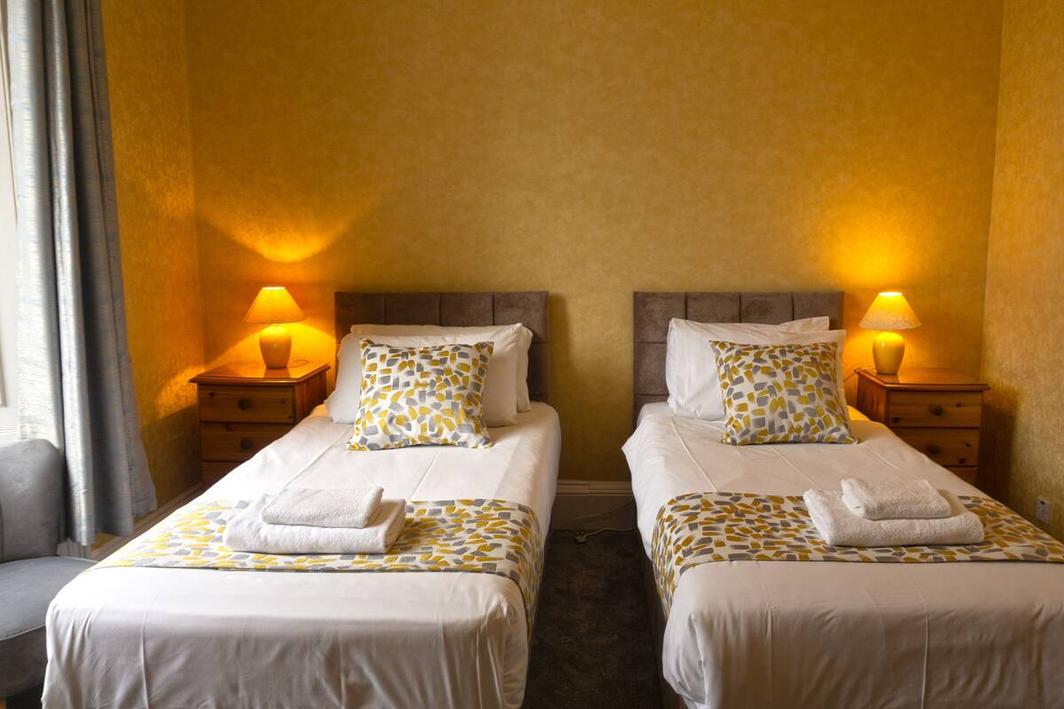 A hotel room with two beds, each with a pillow and a matching pillowcase. There are bedside lamps on wooden nightstands.