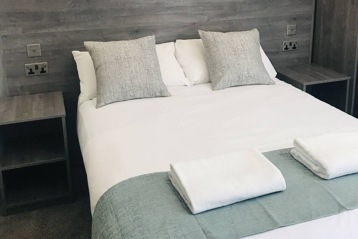 A neatly made bed with a grey headboard, two bedside tables with lamps, and a green throw blanket.