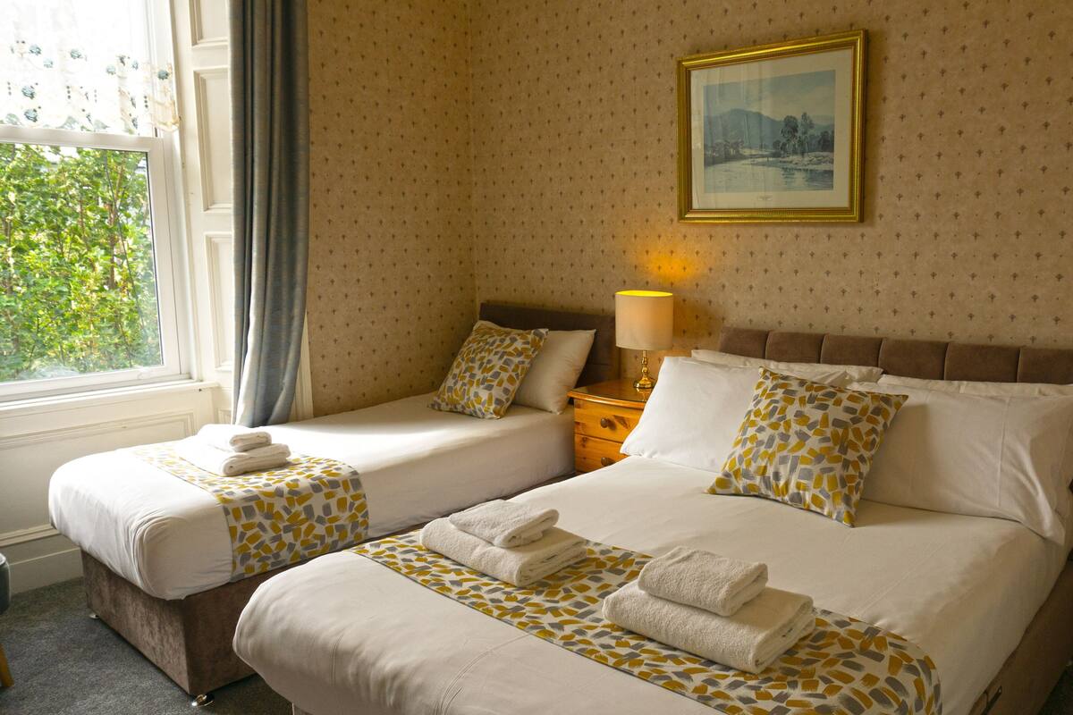A hotel room with two beds, a nightstand with a lamp, and a window with curtains.