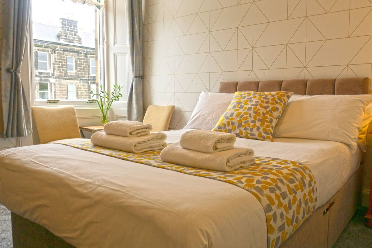 A neatly made bed with towels, a bedside lamp, and a patterned pillow.