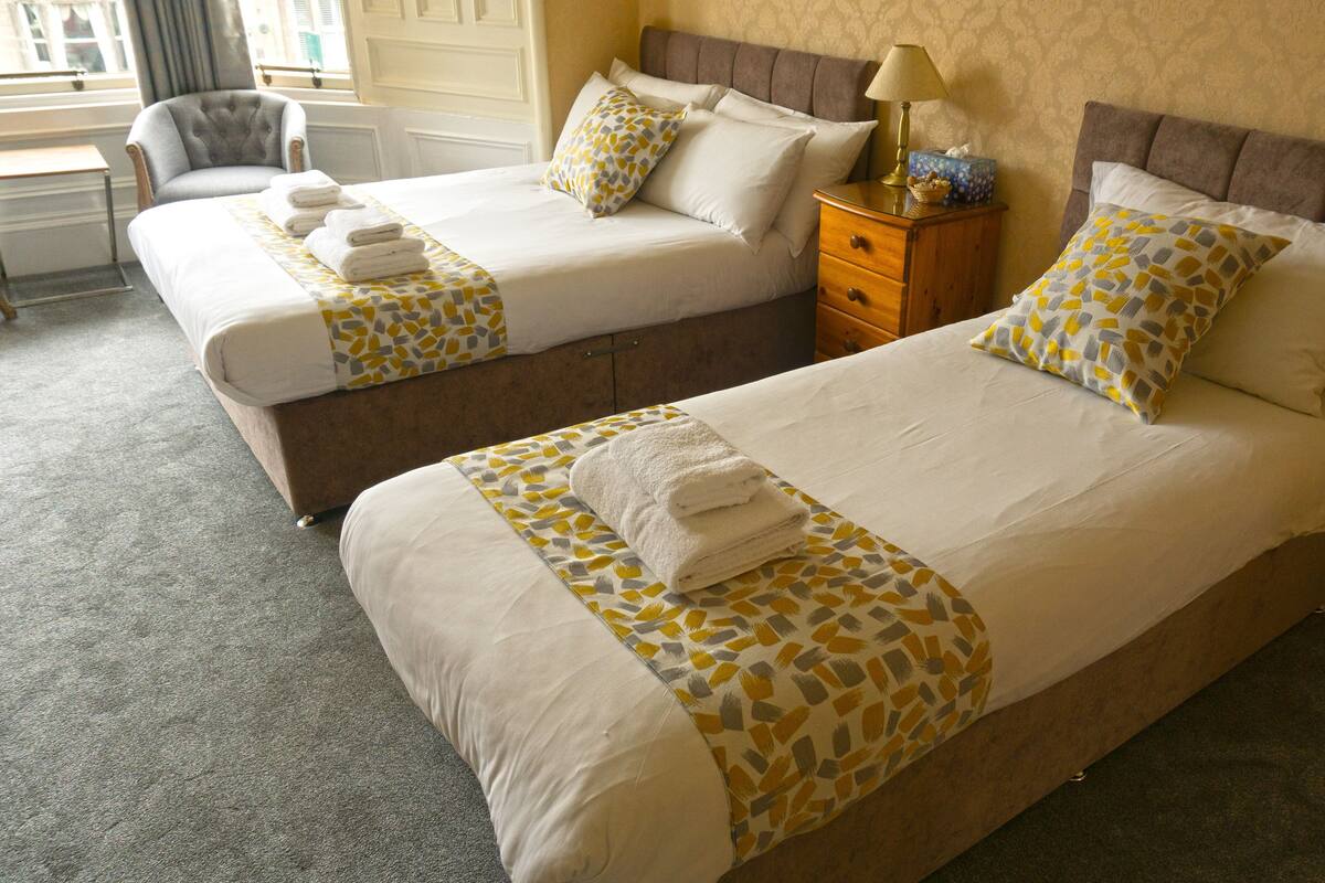 A hotel room with two beds, each with a patterned bedspread and pillows, a wooden nightstand, and a chair.