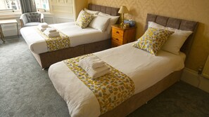 A hotel room with two beds, each with a patterned bedspread and pillows, a wooden nightstand, and a chair. - Arrandale Guest House (Edinburgh)