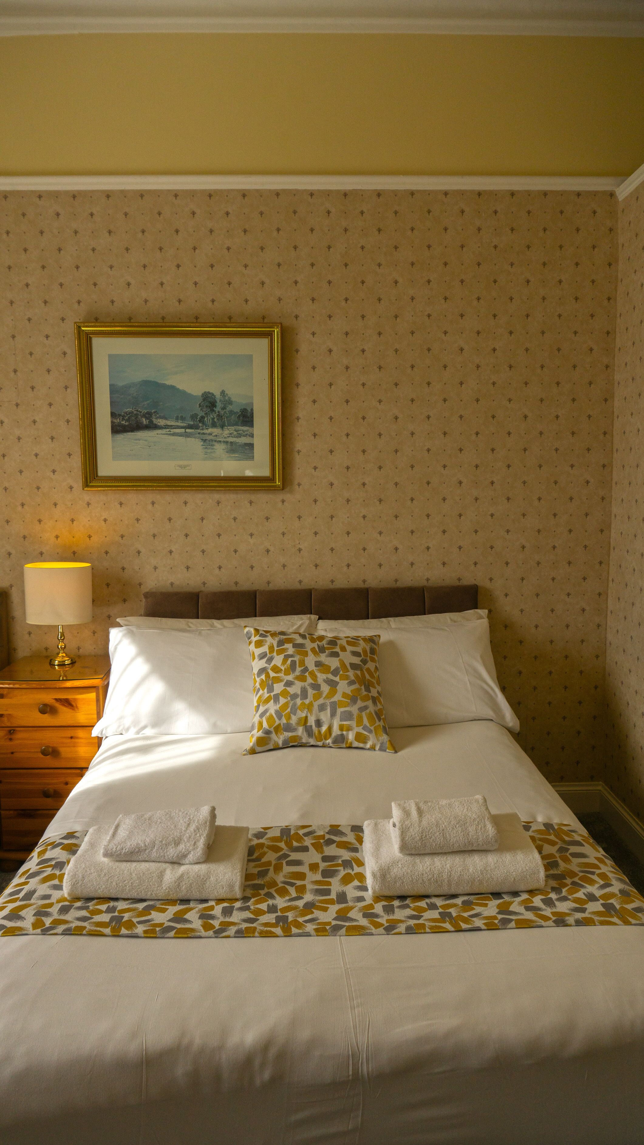 A neatly made bed with white linens and two towels folded at the foot.