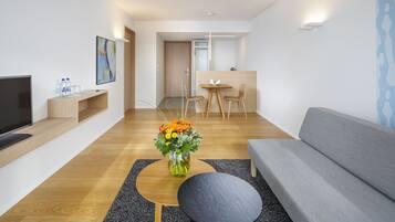 A modern living room with a grey sofa, a wooden coffee table, a black side table, a flat-screen TV, and a vase of flowers.