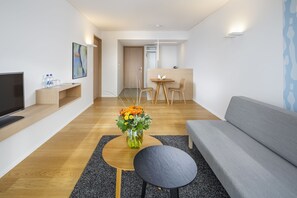 A modern living room with a grey sofa, a wooden coffee table, a black side table, a flat-screen TV, and a vase of flowers. - Hotel NewStar (St. Gallen)