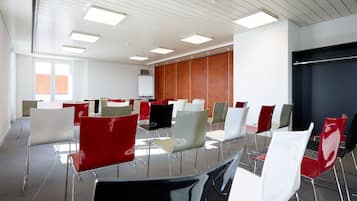 A conference room with a whiteboard, a wooden panel wall, and rows of red, white, and grey chairs.