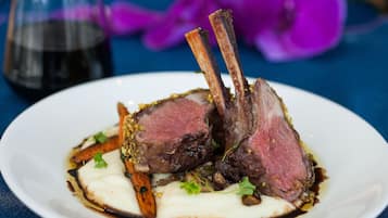 A plate of food with lamb chops, vegetables, and sauce.