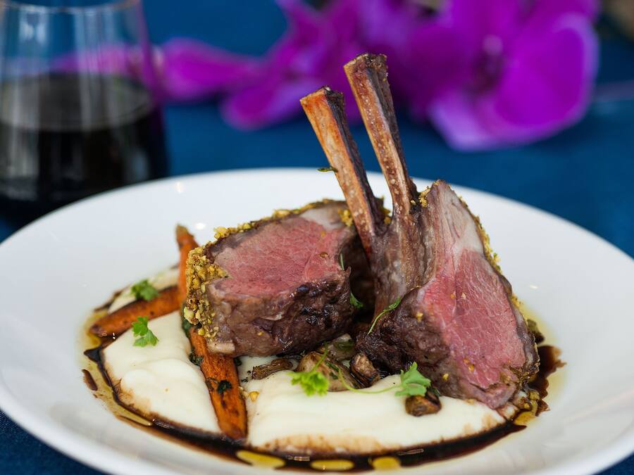 A plate of food with lamb chops, vegetables, and sauce.