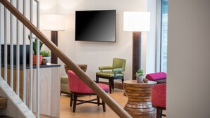 A modern interior with a staircase, a flat-screen TV, two lamps, and a seating area with a round wooden table and chairs. - The Hotel At Oberlin (Oberlin)