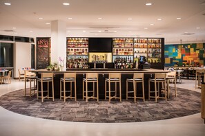 A modern bar area with a central counter, multiple stools, and shelves stocked with bottles. - The Hotel At Oberlin (Oberlin)