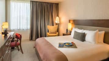 Une chambre d’hôtel avec un grand lit, un bureau avec une chaise, une lampe et une vue sur l’extérieur par une fenêtre munie de rideaux.
