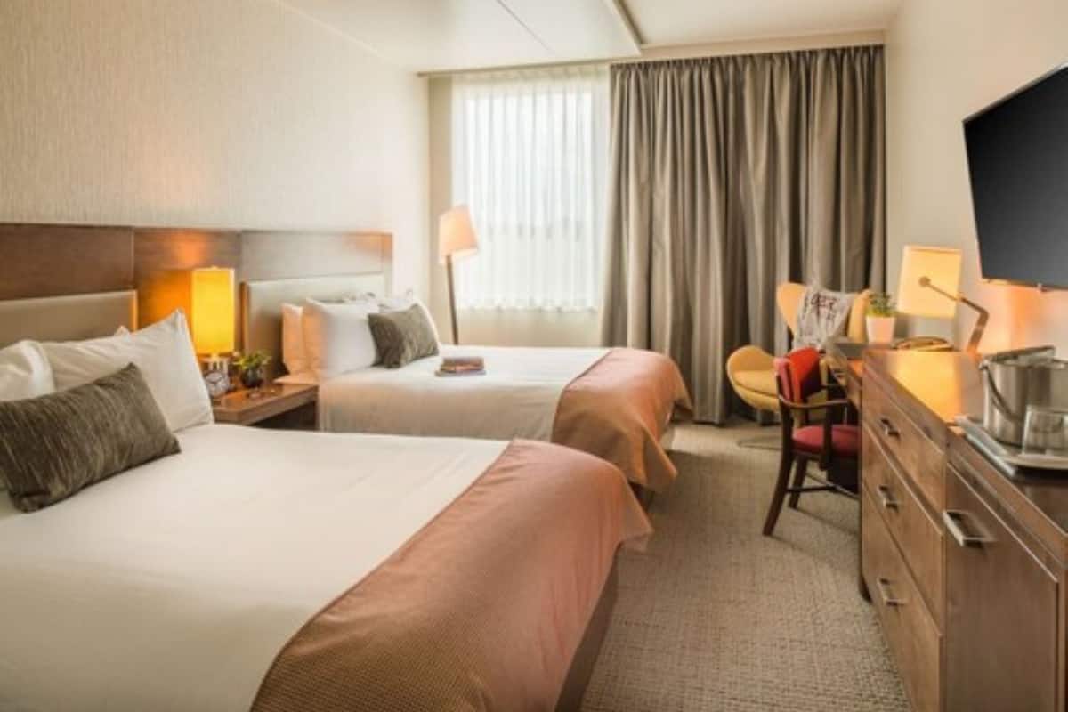 A hotel room with two beds, a desk, a chair, and a television.