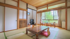 A traditional Japanese room with tatami flooring, a wooden table, sliding doors, and a view of greenery outside. - Kounso (Yamanakako)