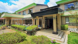 A two-story building with a green roof and beige walls, featuring a covered outdoor seating area with tables and chairs. - Kounso (Yamanakako)