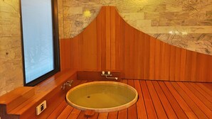 A wooden-floored room with a large oval bathtub, a wooden bench, and a stone wall with a marble-like pattern. - Kounso (Yamanakako)