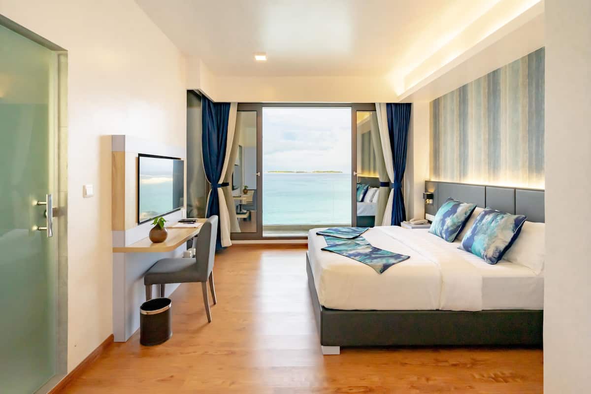 A modern hotel room with a bed, desk, and a view of the sea.