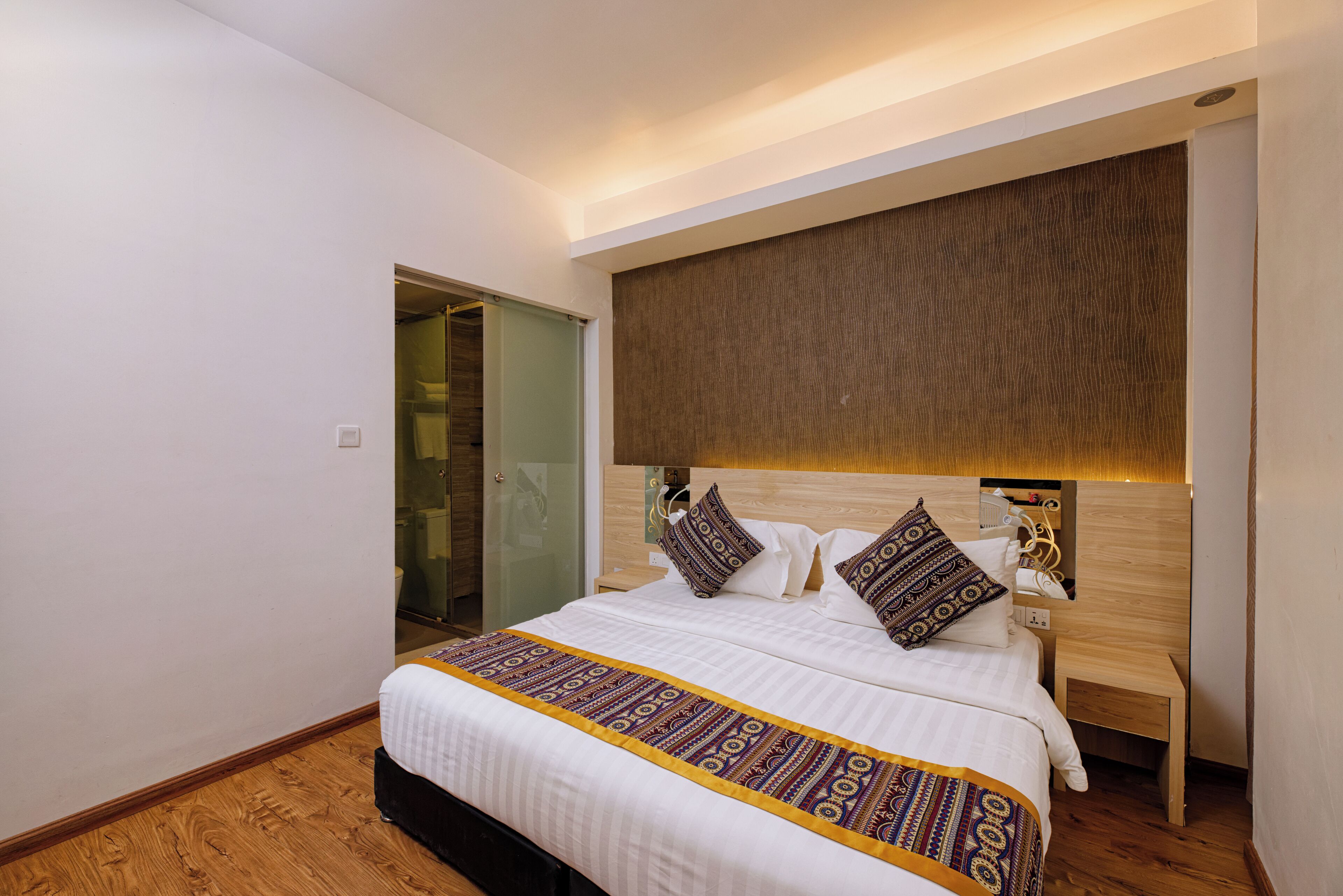 A modern hotel room with a large bed, a wooden headboard, and a nightstand.