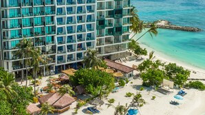 A multi-story hotel with a beachside location, featuring a pool area, beach umbrellas, and a view of the ocean. - Arena Beach Hotel (Maafushi)
