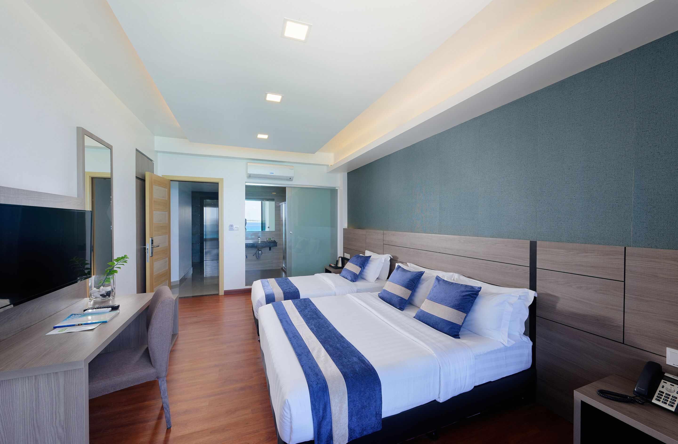 Habitación de hotel con una cama grande, un escritorio con televisor y un baño visible a través de una puerta abierta.