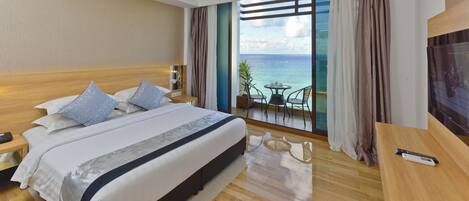 A hotel room with a large bed, a balcony with a view of the sea, a TV, and a small table.