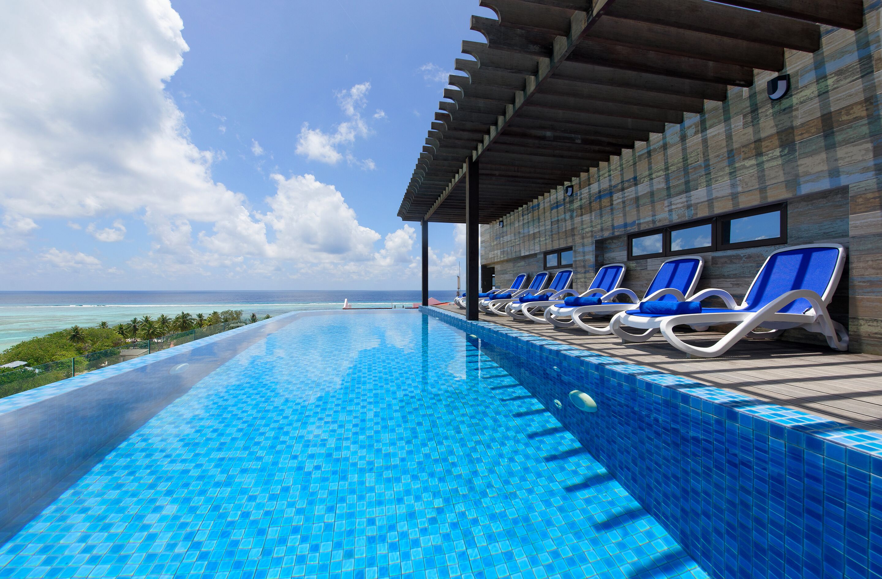 Una piscina con azulejos azules, una zona techada con sillas de descanso y vistas al océano.