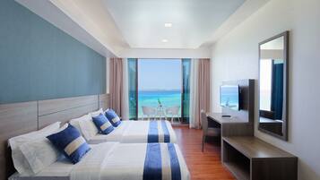Habitación de hotel con dos camas, un escritorio, un televisor y un balcón con vista al mar.