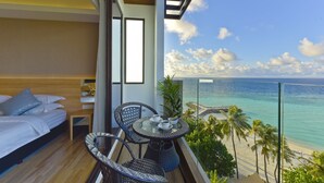 A balcony with a bed, a table with cups, and a view of the beach and ocean. - Arena Beach Hotel (Maafushi)